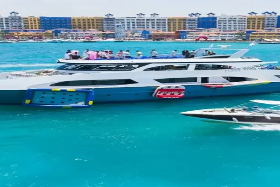 Large luxury yacht and a speed boat cruising the bright blue waters of Porto Marina North Coast, with the colorful resort skyline in the background. 1630 400